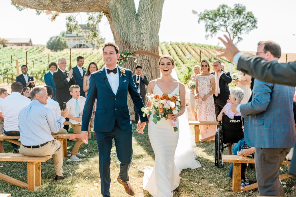 Bride and groom, exit their wedding ceremony, laughing at Ellas Vineyard in Paso Robles, California.