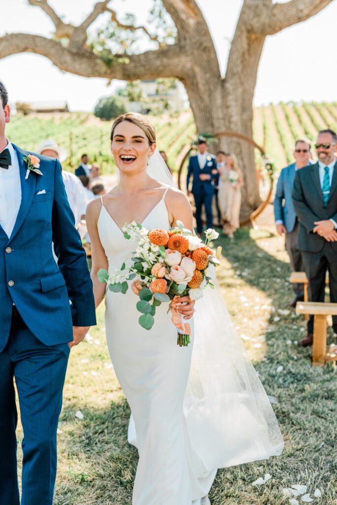 A candid moment of the bride, laughing as she walks out of her wedding ceremony at Ellas Vineyard in Paso Robles.