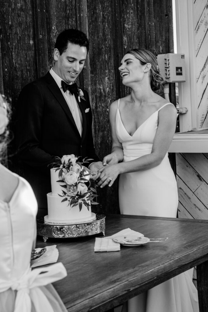 A bride and groom lap as they cut their wedding cake during their Ellas Vineyard wedding reception in front of the barn. 