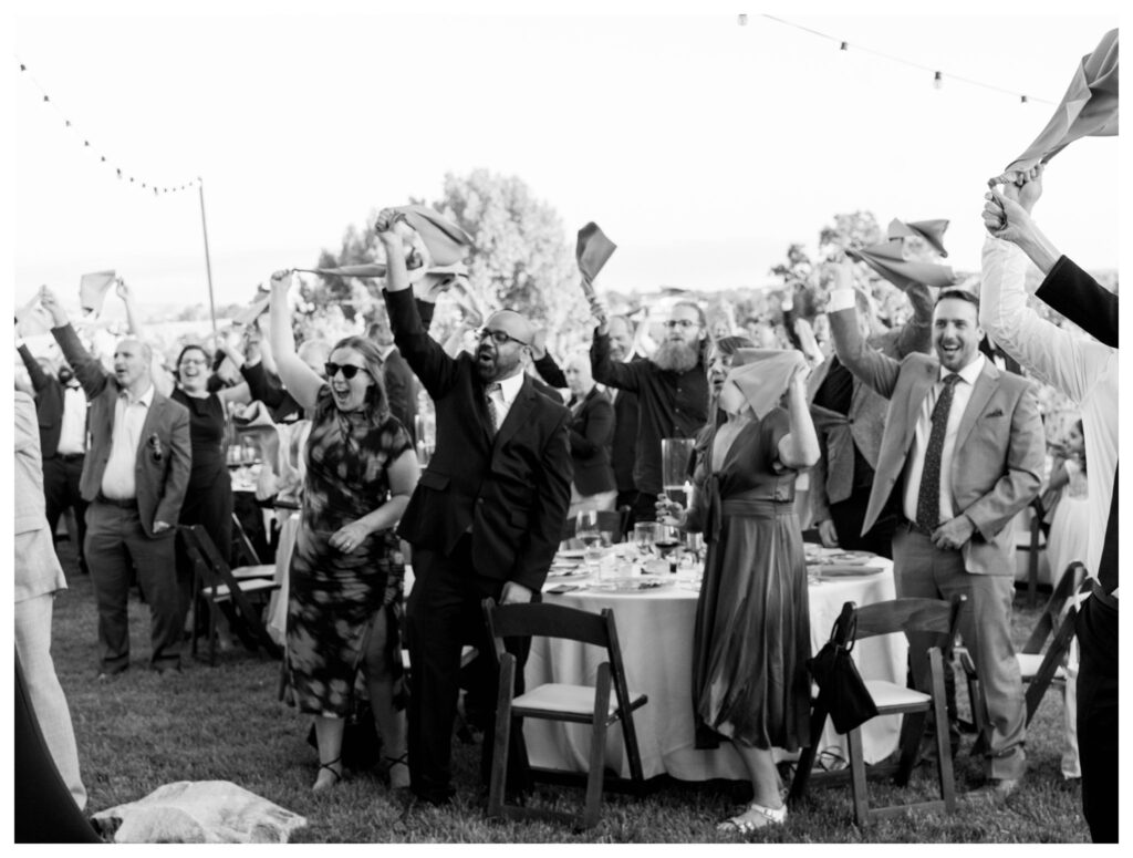 Guests cheering with napkins in celebration at lively vineyard wedding reception in Paso Robles by Leana Myra Photography