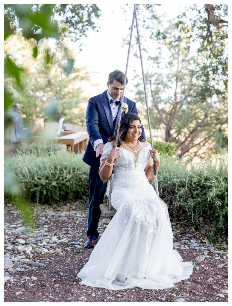 Charming portrait of bride on rustic swing with groom at romantic Paso Robles vineyard wedding captured by Leana Myra Photography.