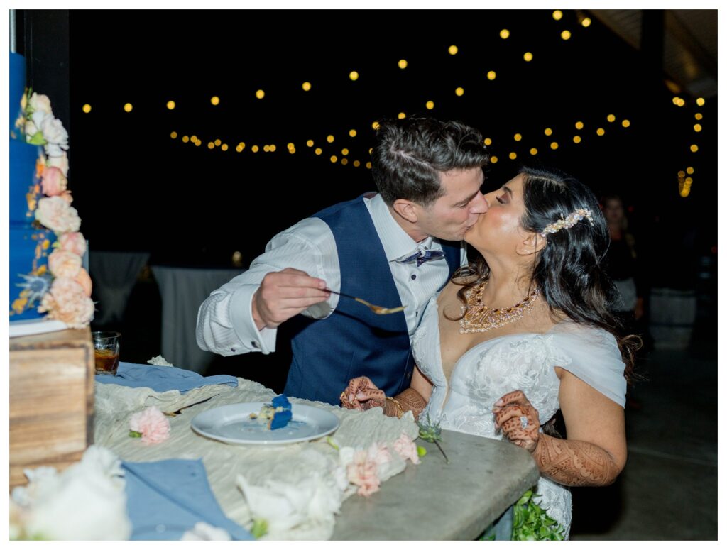 Bride and groom sharing a romantic kiss while cutting cake under string lights at their Paso Robles vineyard wedding, photographed by Leana Myra Photography.