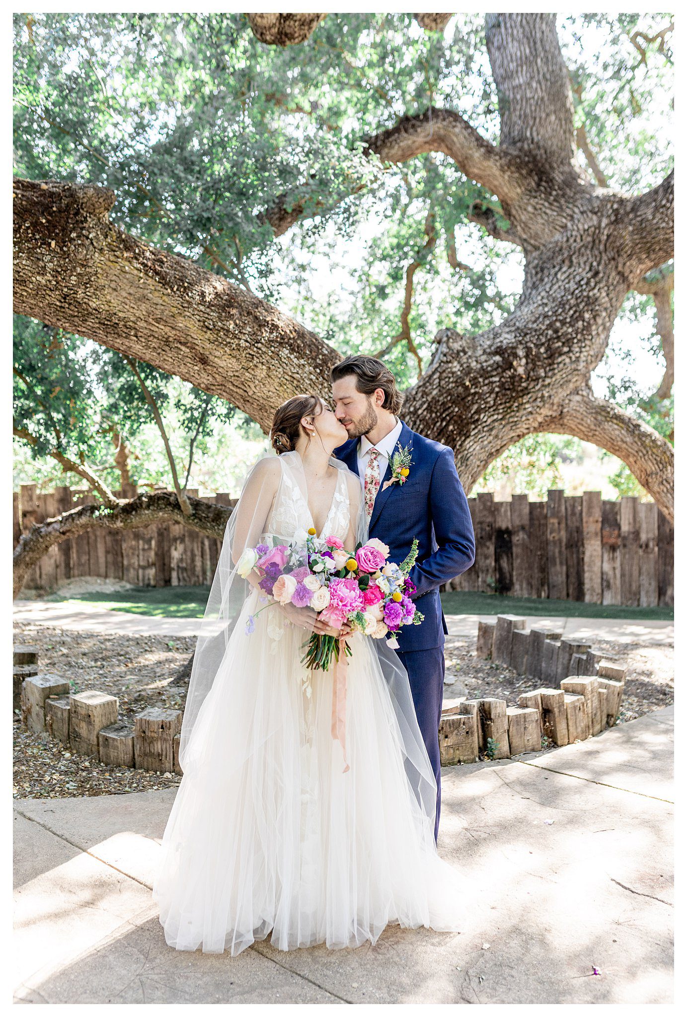 A bride and groom kiss under the oak tree at Hartley farms, a san luis obispo garden wedding venue. 