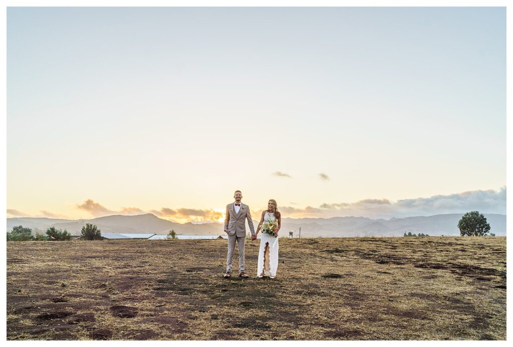 Bride and groom pose together under a gorgeous sunset in a field at Flying Caballos Ranch, a san luis Obispo vineyard wedding venue.