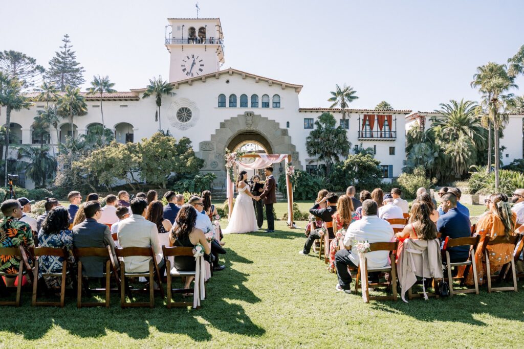 Couple getting married on the terrace at the Santa Barbara Courhoudsw during a large wedding and arch and chairs