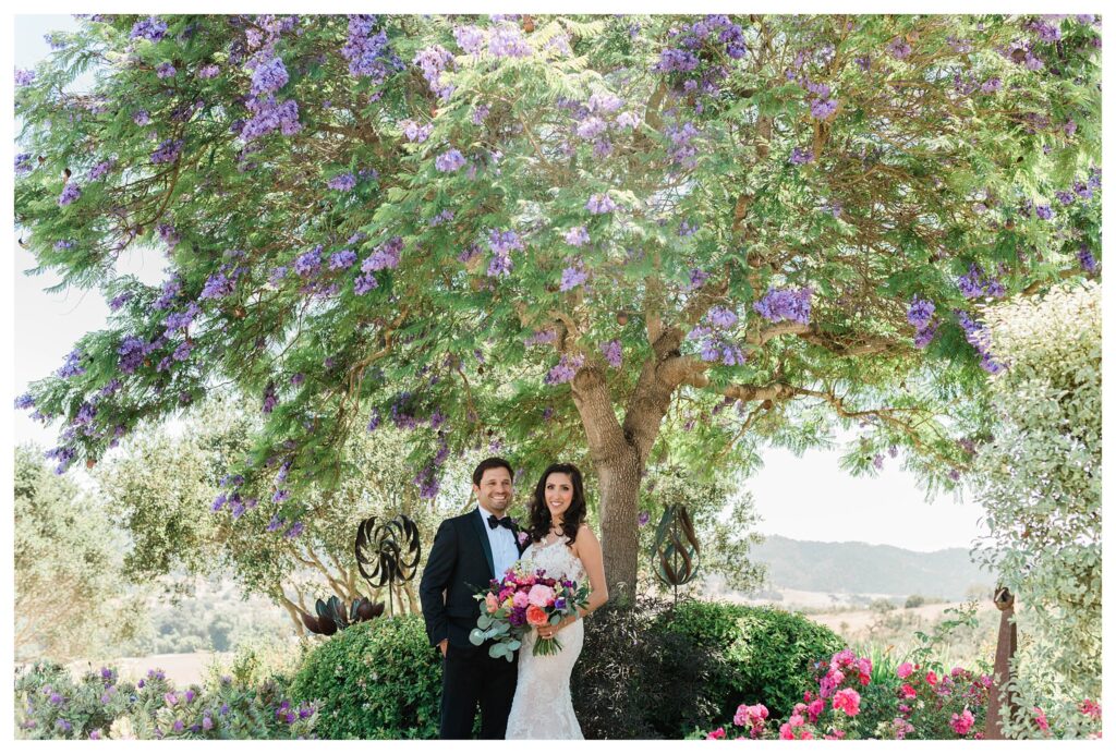 A bride and groom in wedding attire with the bride holding a bright colorful bouquet of flowers for their during garden wedding at the Casitas Estate in San Luis Obispo, an outdoor wedding venue.