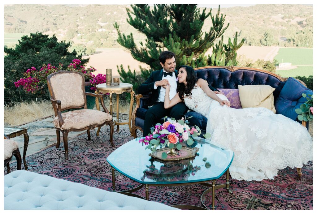 A bride and groom in elegant wedding attire recline on sofas at their Persian wedding at the Casitas Estate a luxury garden wedding venue in san Luis Obispo.