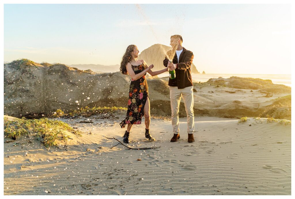 And engaged couple laughs as they pop a bottle of champagne on top of a Sandune at their Central Coast engagement session.