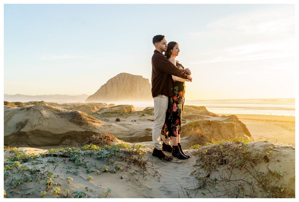 Hold the woman passionately as they stand on a Sandune overlooking the Morro Bay rock during their engagement pictures, and the San Luis Obispo, California.