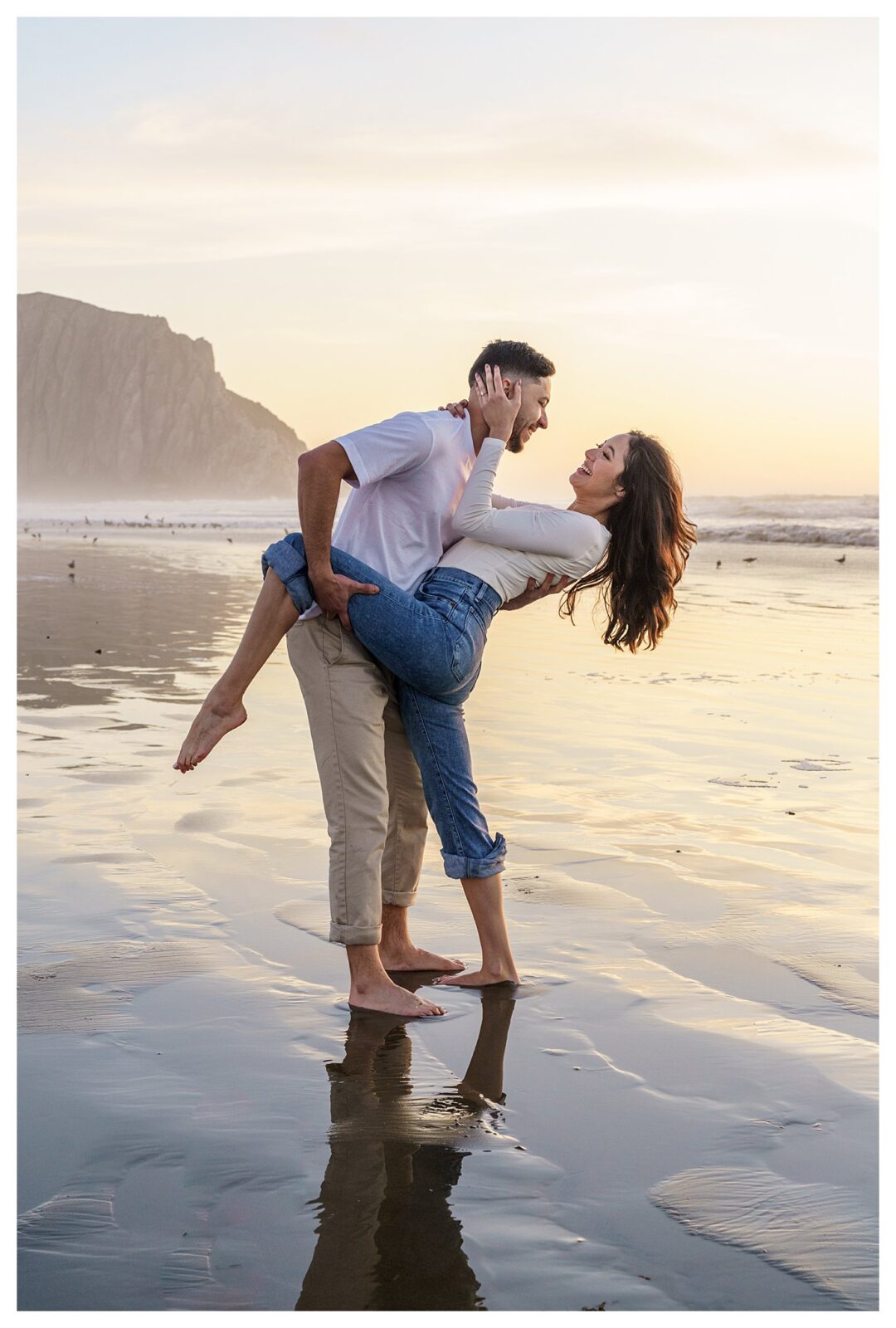 Morro Bay Beach engagement session, with a man, laughing as he dips a woman back in the waves during their engagement pictures, this is a great example of a perfect engagement session pose.