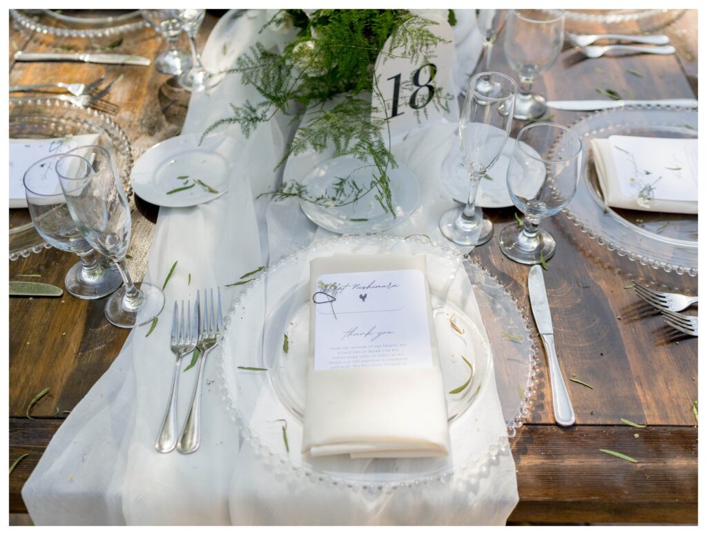 Glass plate, greenery, and thank-you note on wooden table at Maravilla Gardens reception.

