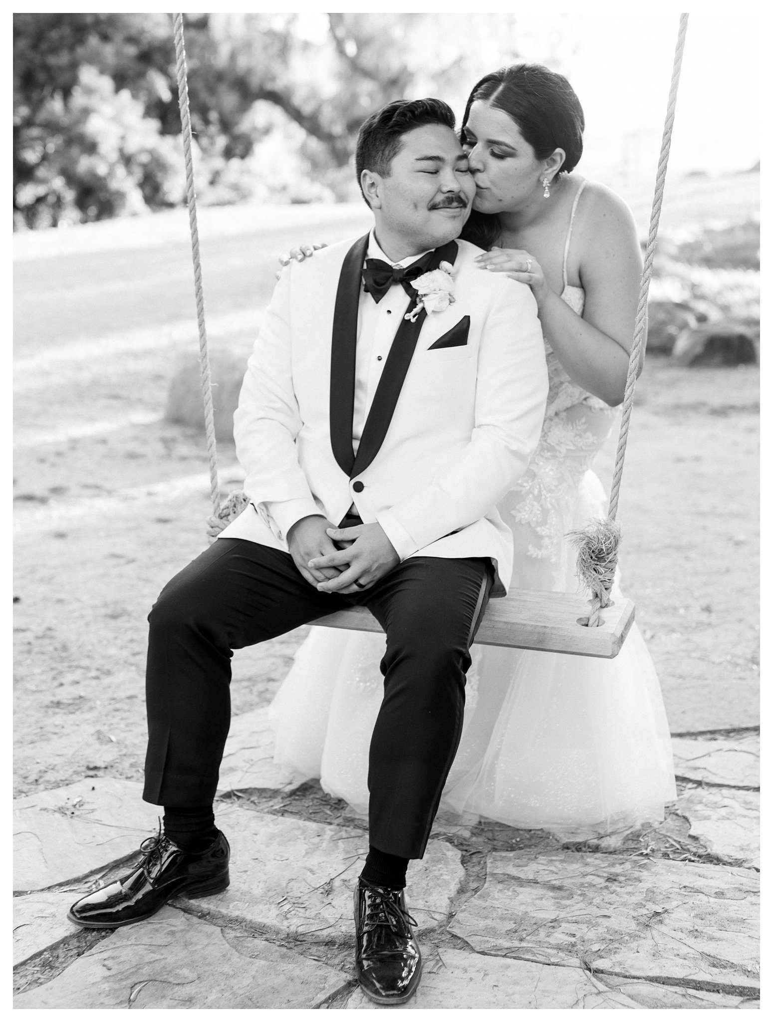 Black and white photo of bride kissing groom on rustic swing at Maravilla Gardens in Camarillo.

