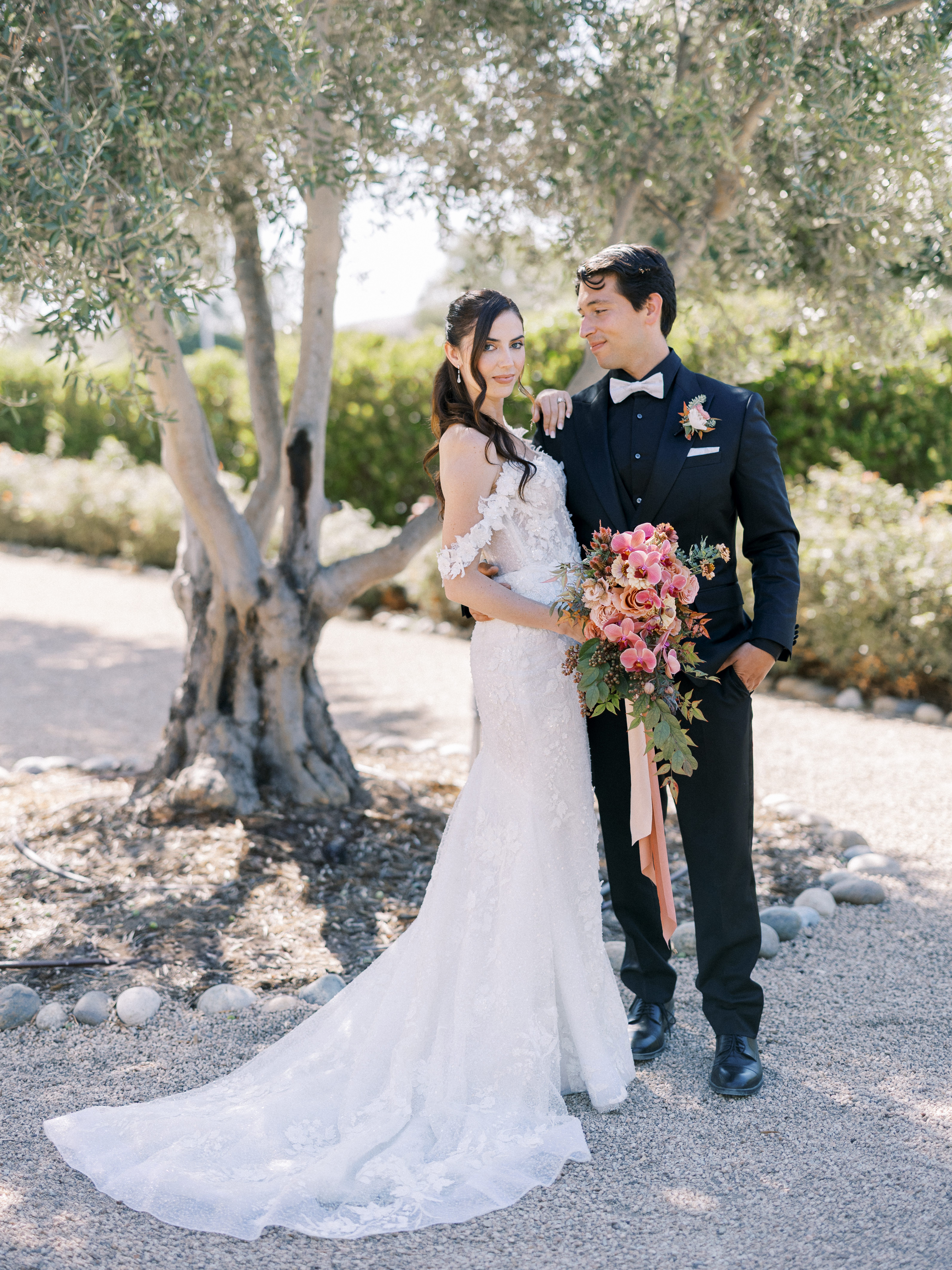 Elegant bride and groom with cascading pink bouquet in a sunlit garden setting