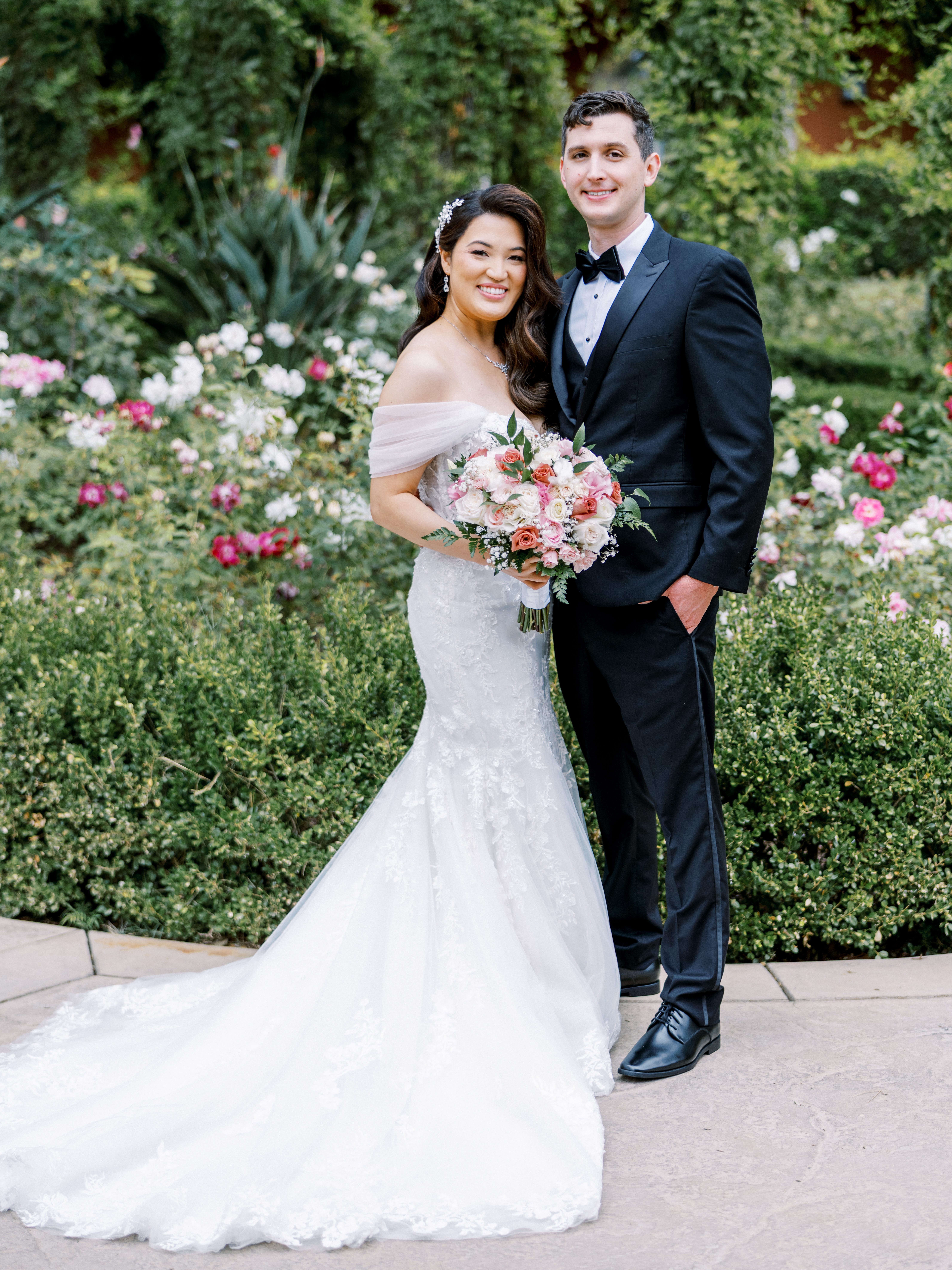 Bride and groom smiling in a lush rose garden on their wedding day