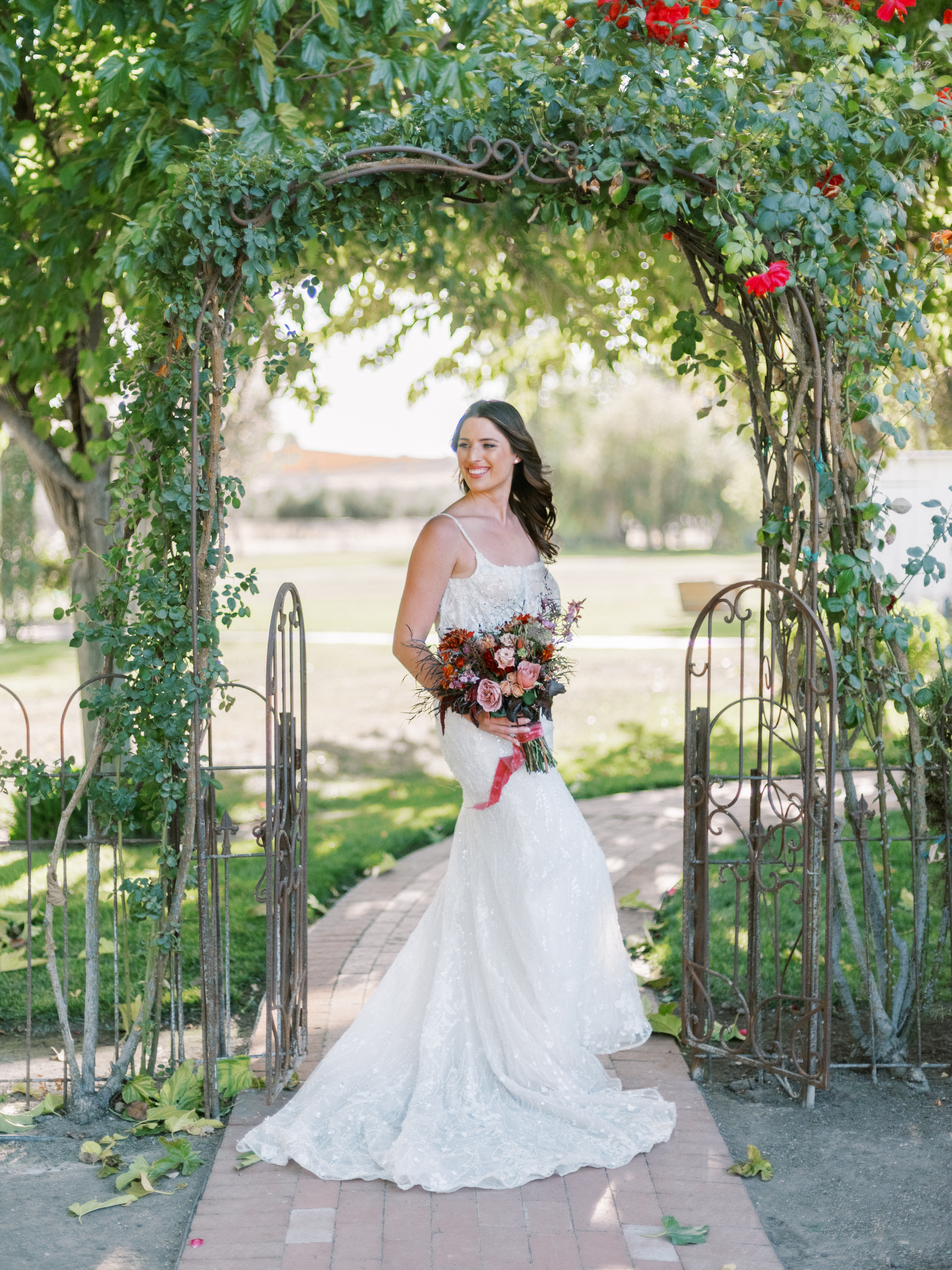Bride walking through garden gate with autumn-toned bouquet and lace gown
