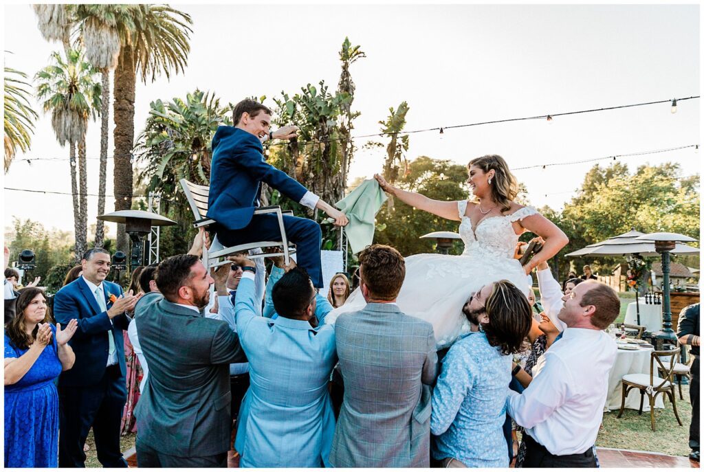 The bride and groom laugh as they are lifted on chairs during a traditional Jewish dance at the Santa Barbara zoo during their wedding reception.