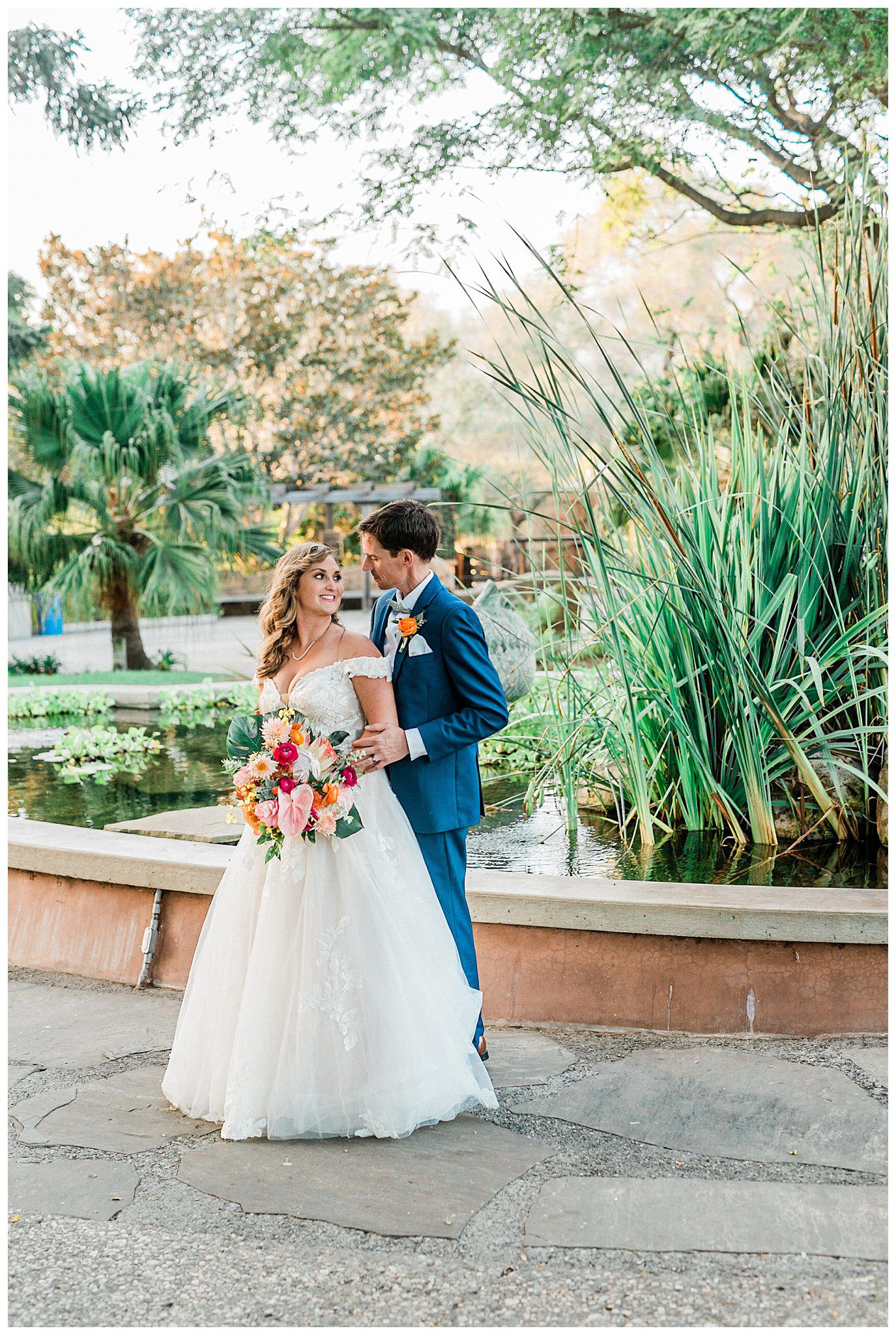 A bride and groom in front of the pond at the Santa Barbara zoo, surrounded by tropical and botanical flowers.