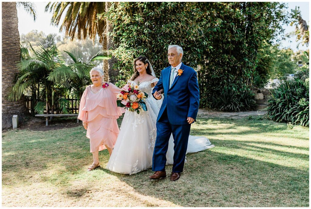 A bride walks with her father down the ceremony aisle at the Santa Barbara zoo on her wedding day.