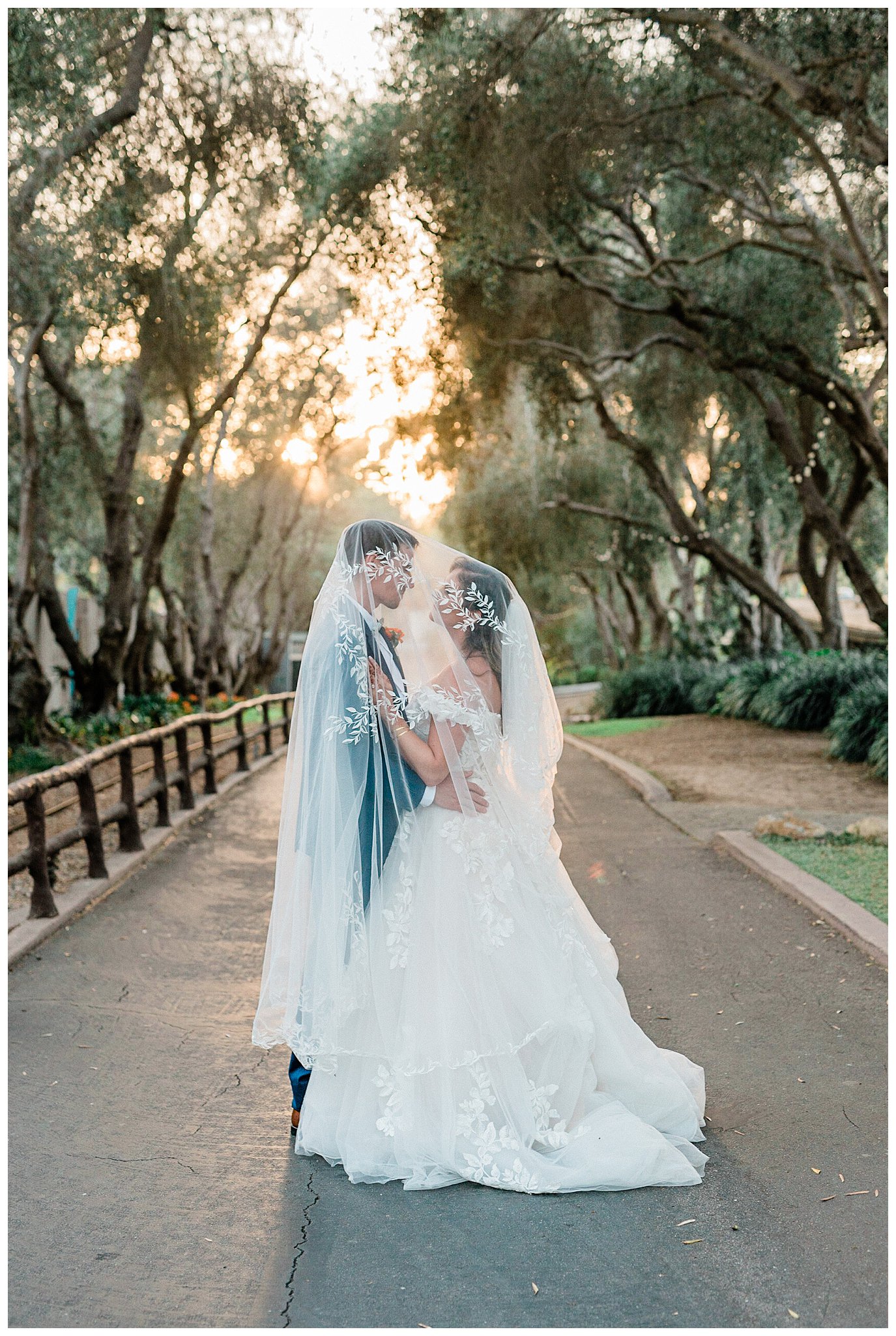 A bride and groom stand under the wedding veil with golden warm light, flowing through the trees during their wedding at the Santa Barbara zoo, a unique California wedding venue.