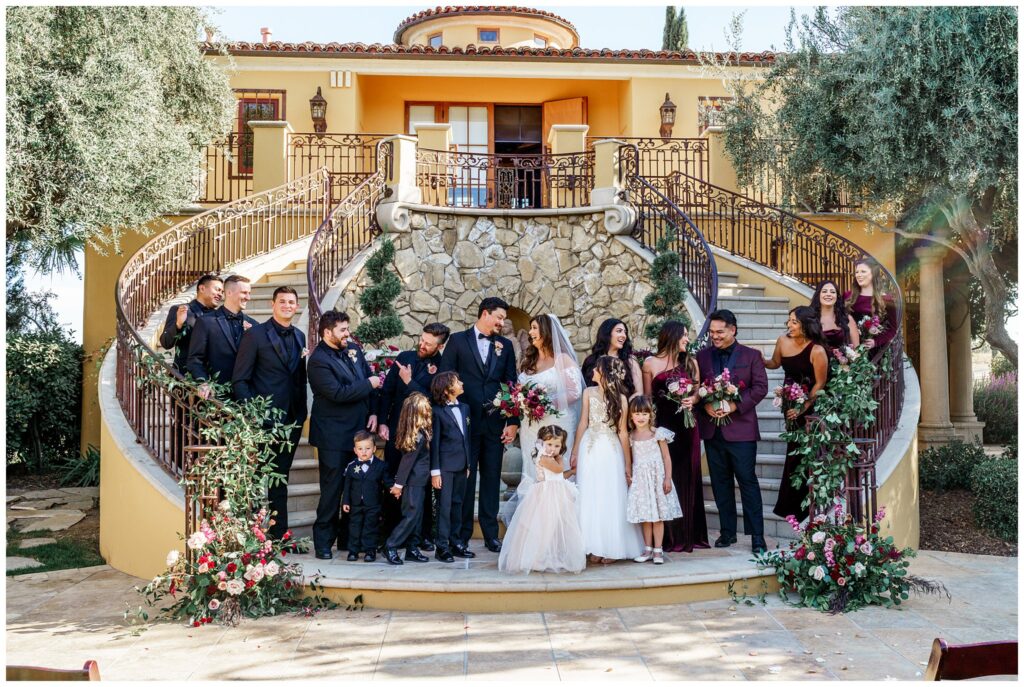 A bride and groom in wedding decor stand on the stairs for a photograph with their wedding party during their wedding at Cali Paso, Villa, and winery in Paso Robles, California.