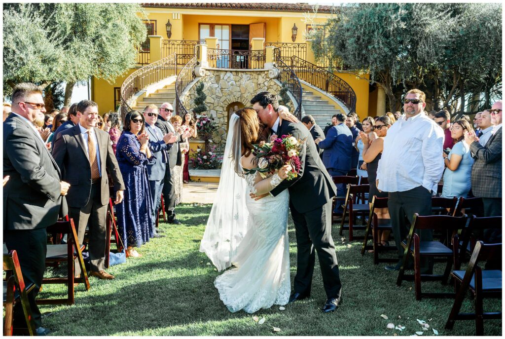 A bride and groom kiss as they walk down the aisle on their luxury wedding day at Cali Paso, winery, and Villa.