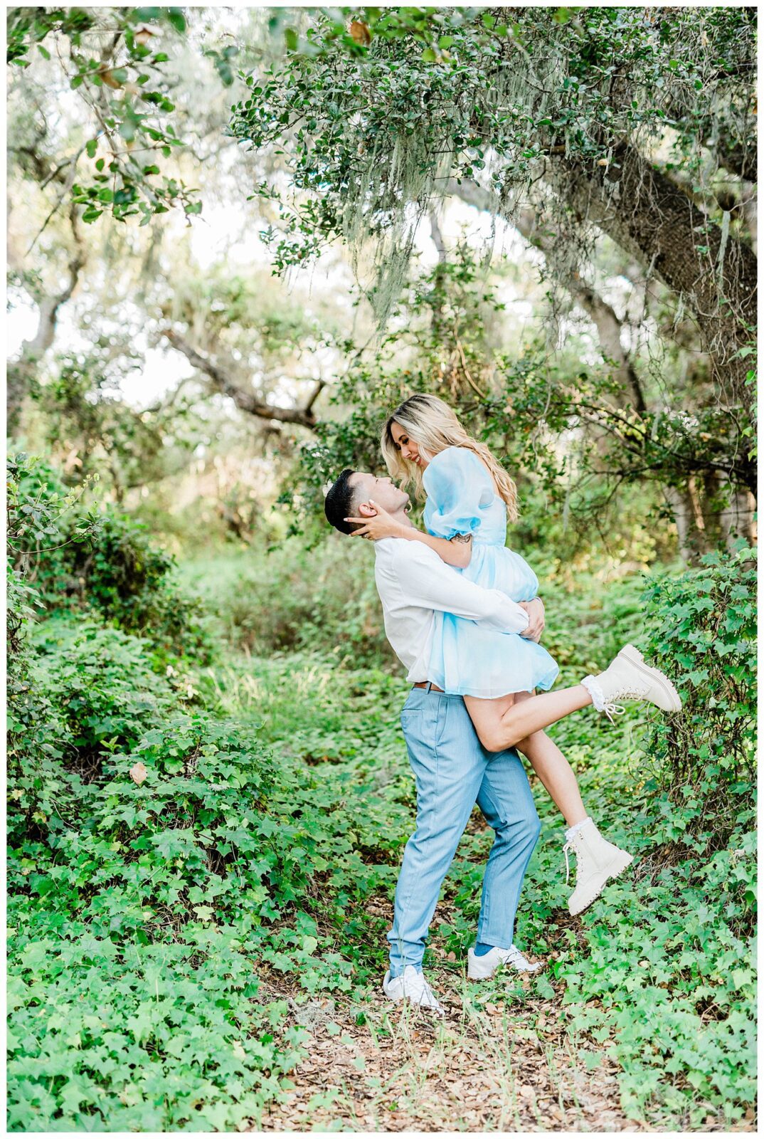 A fun and whimsical moment between an engaged couple during their central coast engagement session as the groom lifts the bride into their air and they laugh for an engagement pose. 
