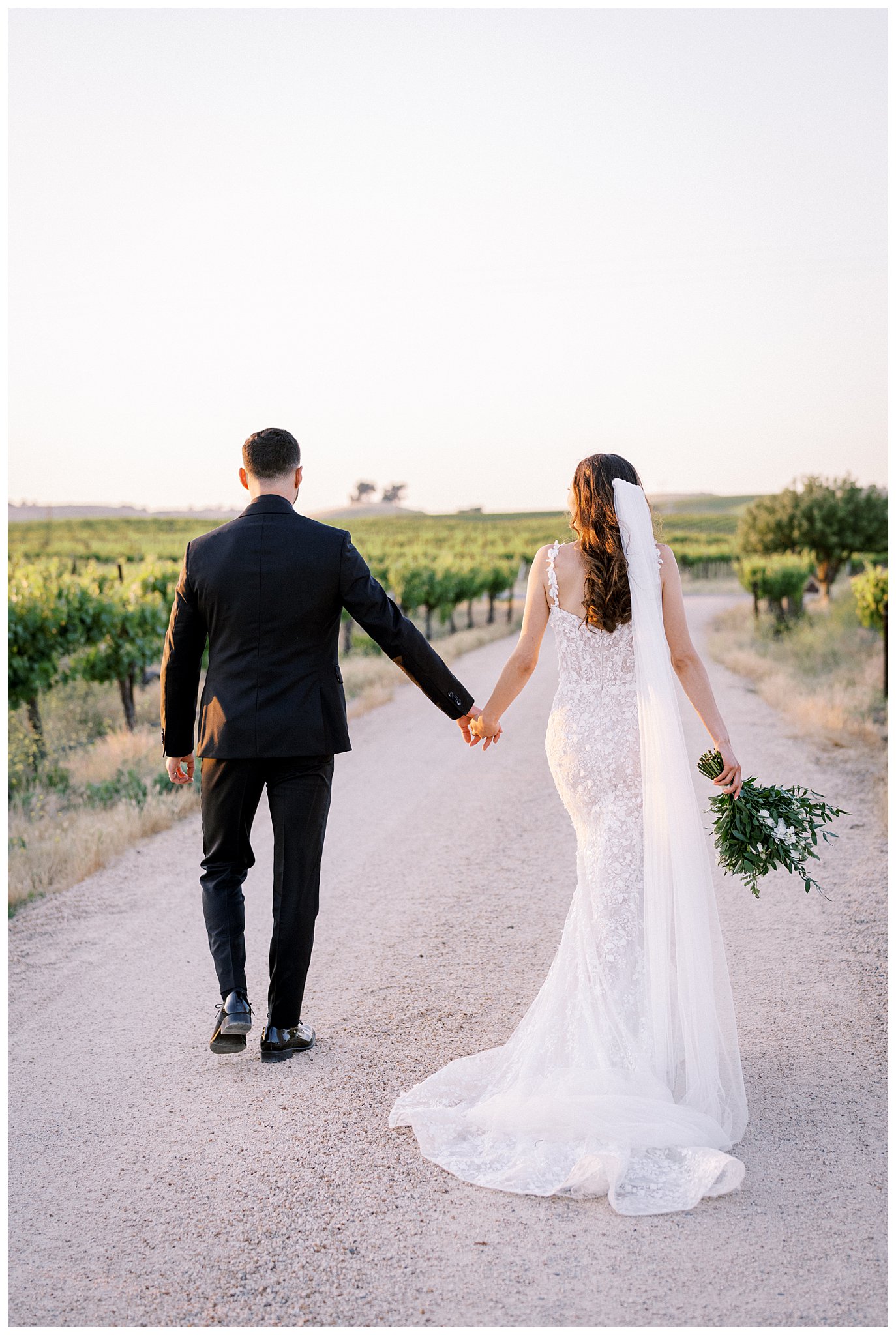 A bride and groom walk through the vineyards during their luxury wedding day at Bella Terra Vineyards, in Paso Robles, California.