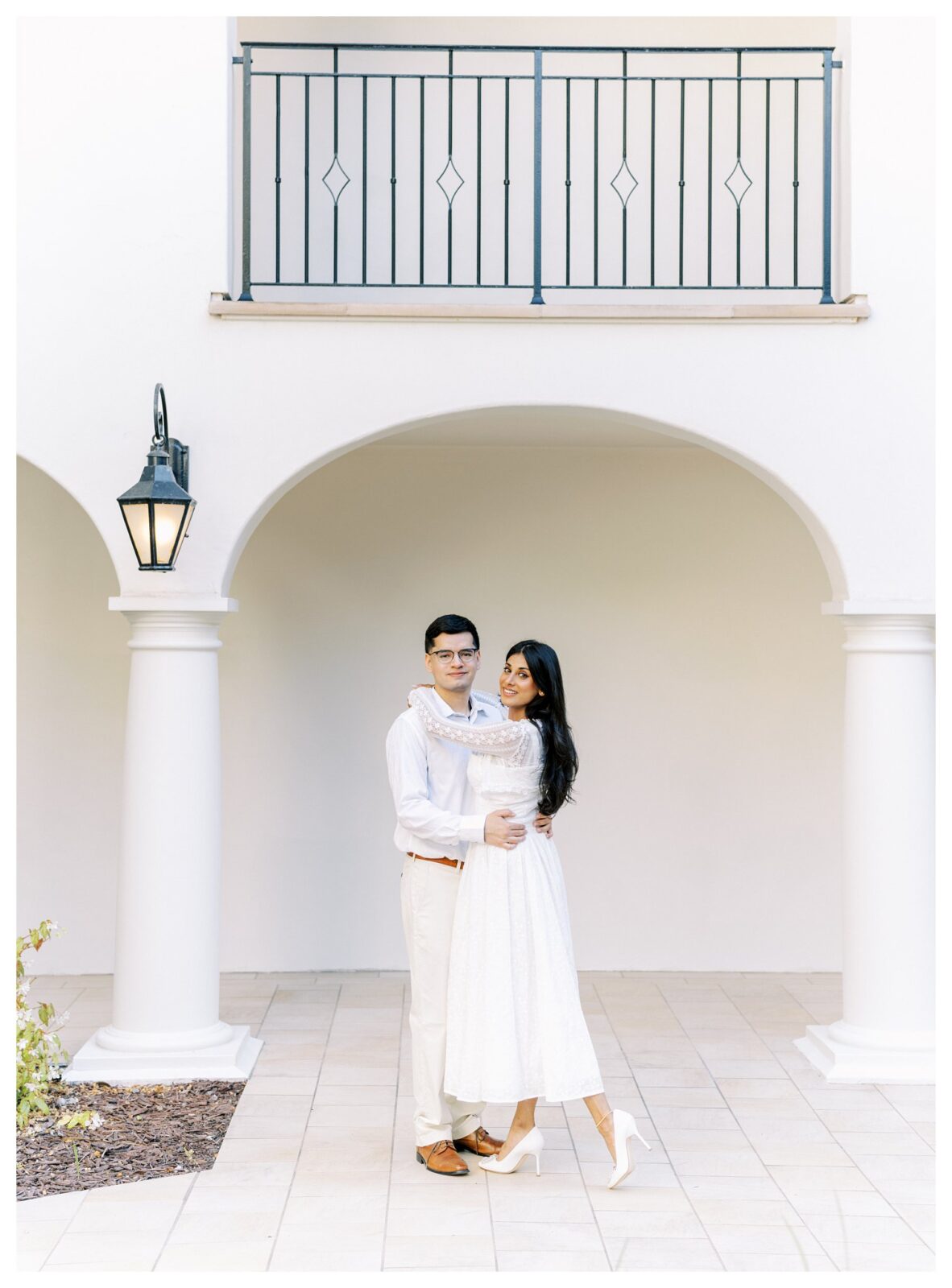 Engaged couple embracing under Spanish-style arches at the Santa Barbara Courthouse in timeless white outfits