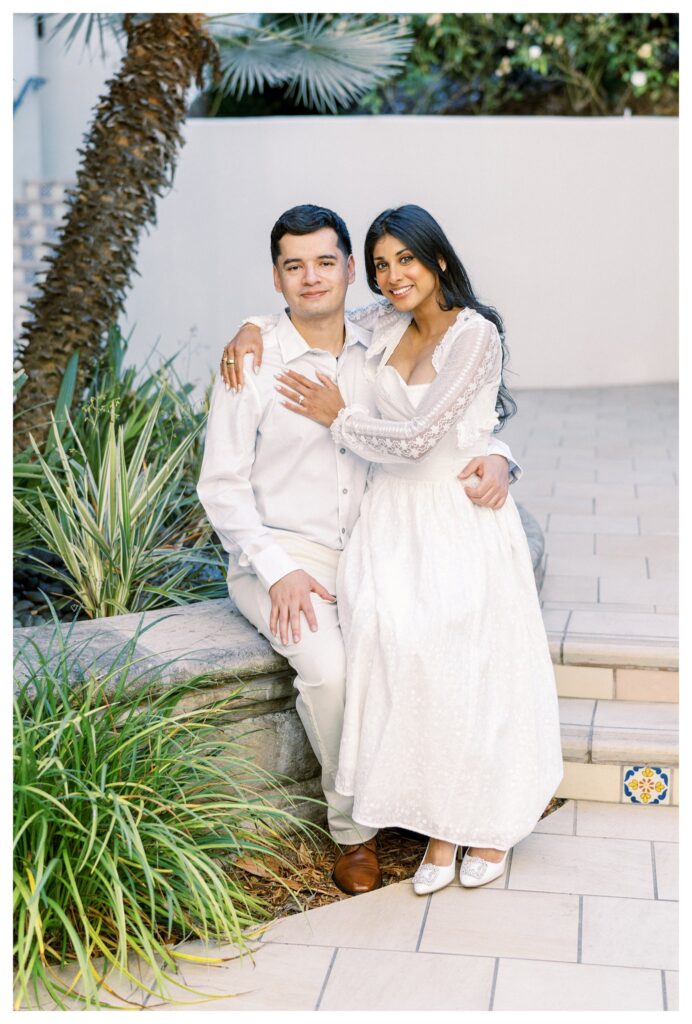 Engaged couple posing on stone steps surrounded by palm trees at the historic Santa Barbara Courthouse gardens