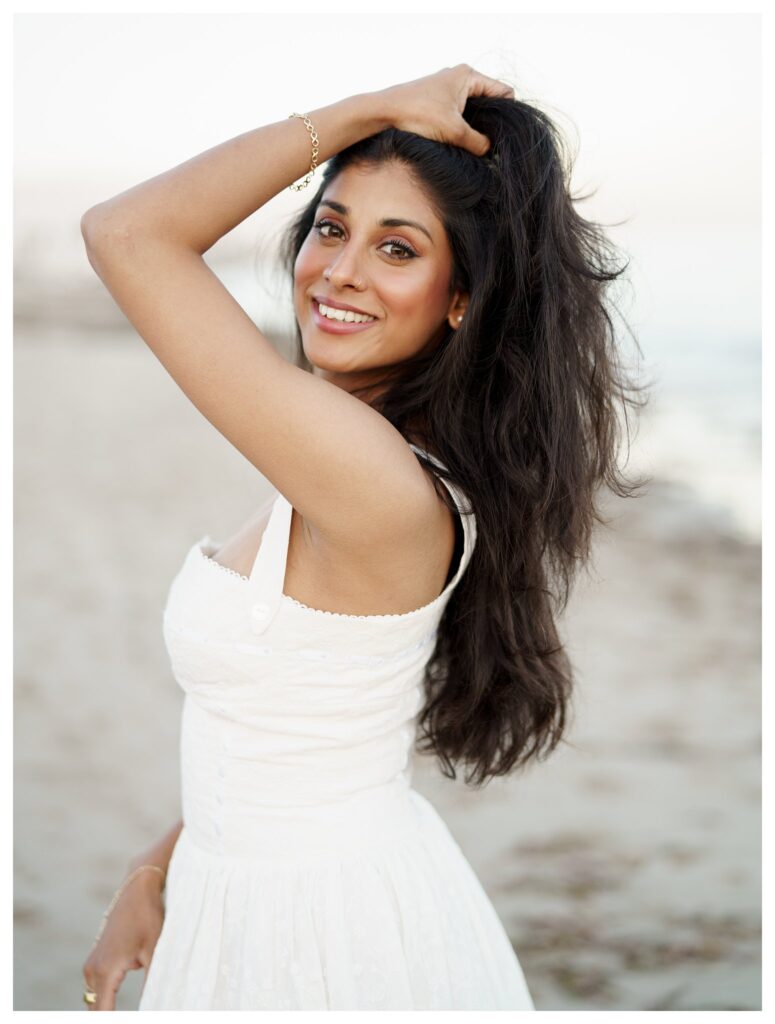 Bride-to-be in classic white eyelet dress smiling over shoulder at Leadbetter Beach during sunset