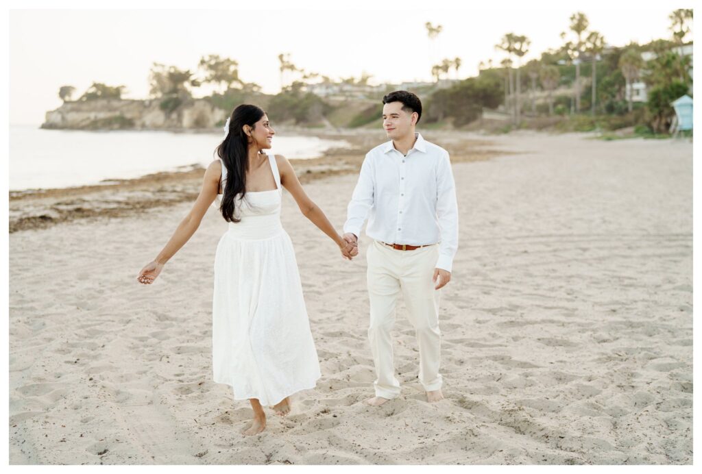 Couple barefoot on the sand at Leadbetter Beach during sunset while smiling back at each other